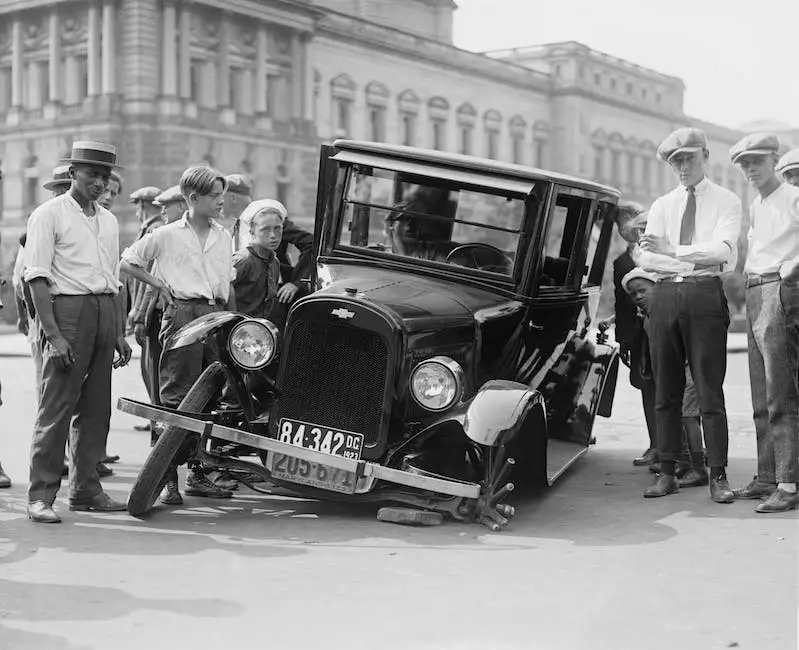 Image depicting a person standing beside a broken down car on the side of the road